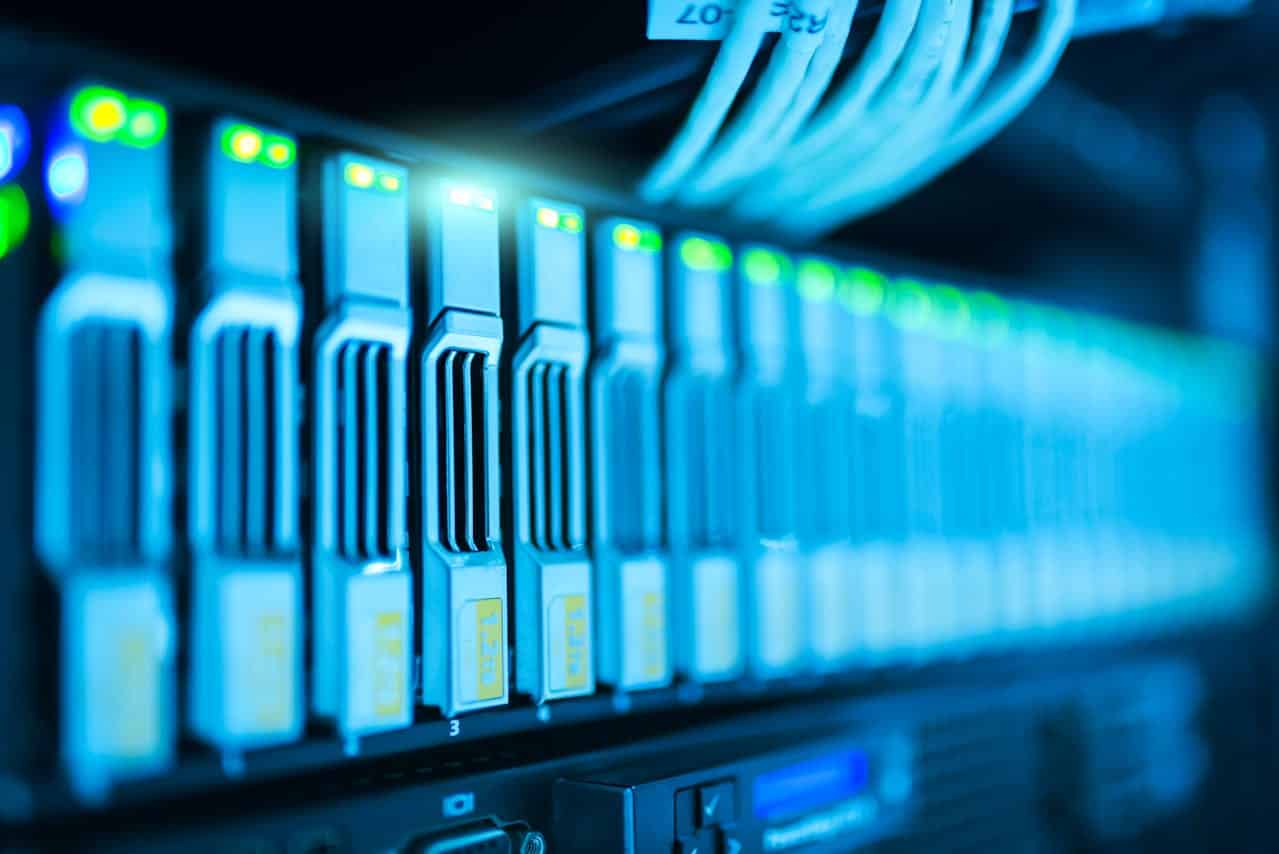 Close-up of illuminated network server hardware with multiple cables plugged in and blue-lit server drives, showcasing the importance of strong defenses in a data center—prompting the question: What is network security?.