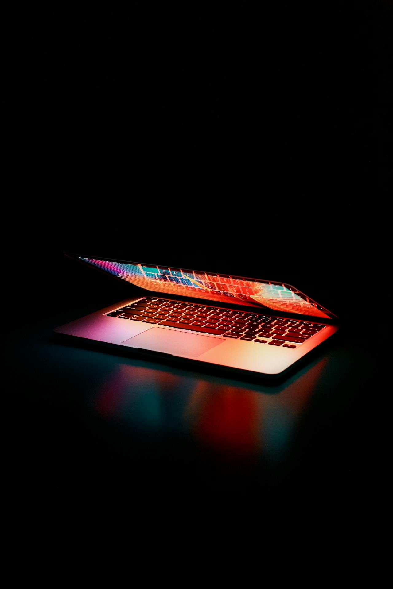 A partially open laptop glows with vibrant, multicolored lights from its screen and keyboard, creating a dramatic effect against a dark background—an iconic image for an innovative IT support company.
