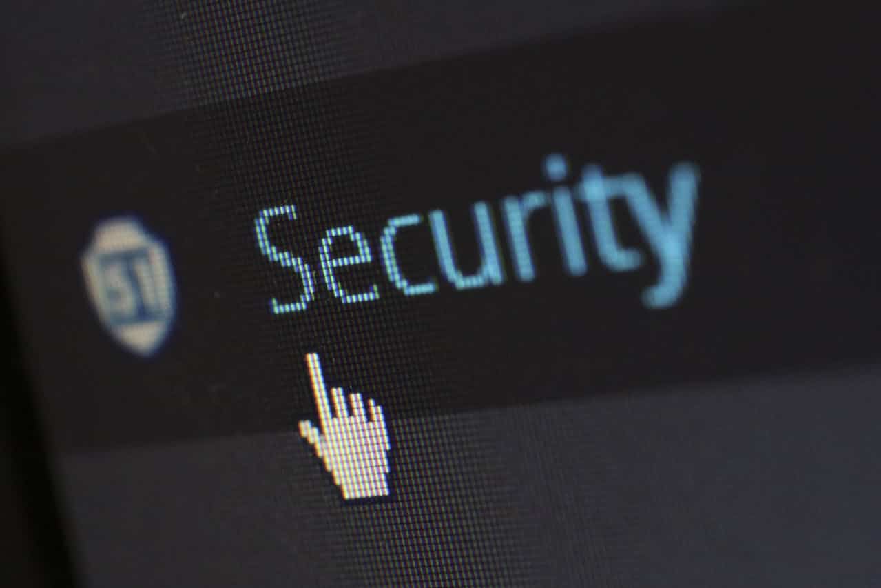 A computer screen displays the word Security next to a shield icon, with a white hand-shaped cursor pointing at the text—prompting viewers to consider, What is network security and how can it protect your system?.
