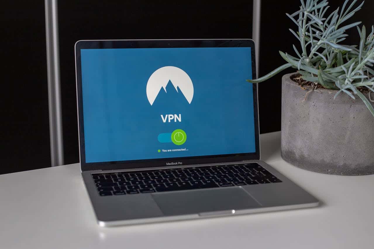 A laptop on a white desk displays a VPN connection screen, highlighting network security. Beside it is a gray pot with a spiky succulent plant. The VPN status shows “You are connected.” with a green check mark.
