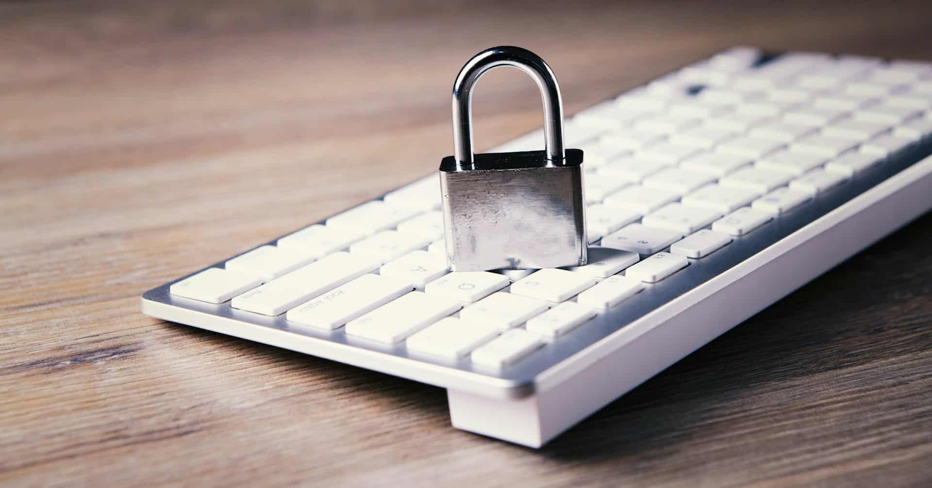 A silver padlock sits on top of a white computer keyboard on a wooden surface, symbolizing cybersecurity, data protection, and Top Tips For Home Office Security.